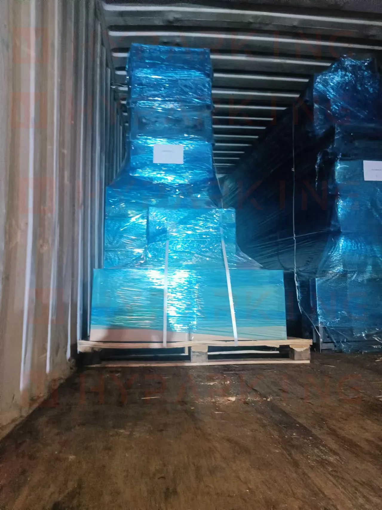 Pallets of parking system components wrapped in protective blue film inside the container